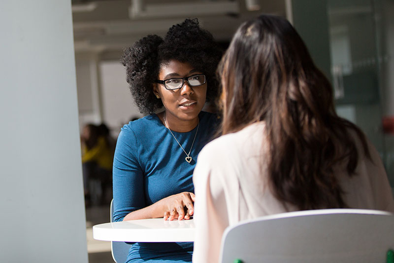 over the shoulder photo of two women talking across a white table