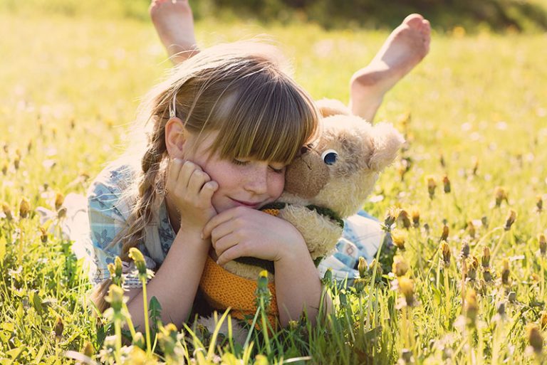 young girl laying in sunny field holding teddy bear